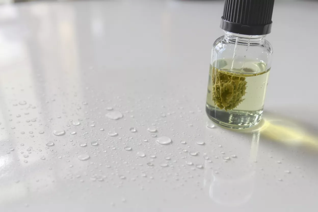 A glass bottle of essential oil with droplets around it