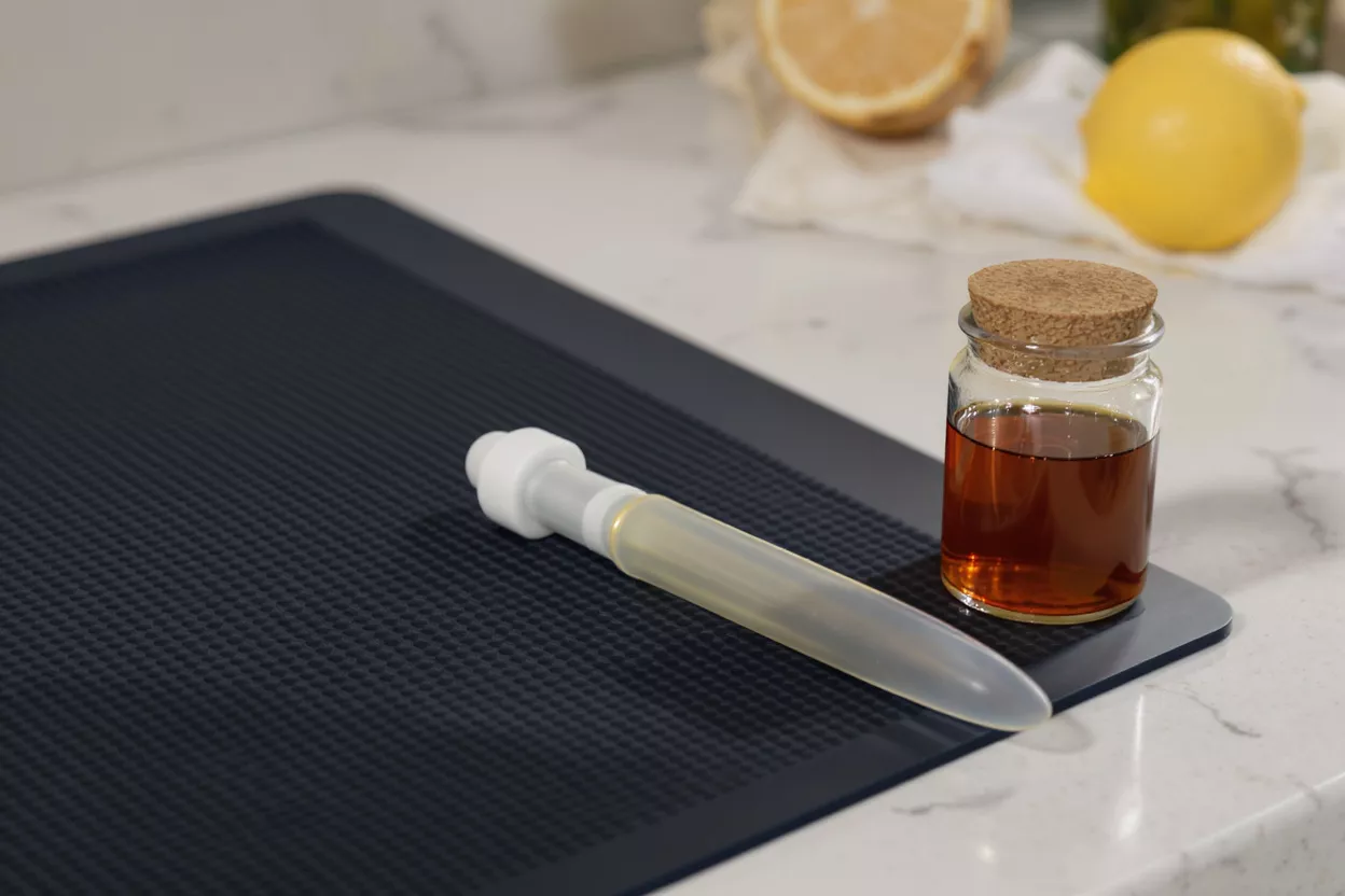A silicone baster and a glass jar of marinade on a textured kitchen mat.