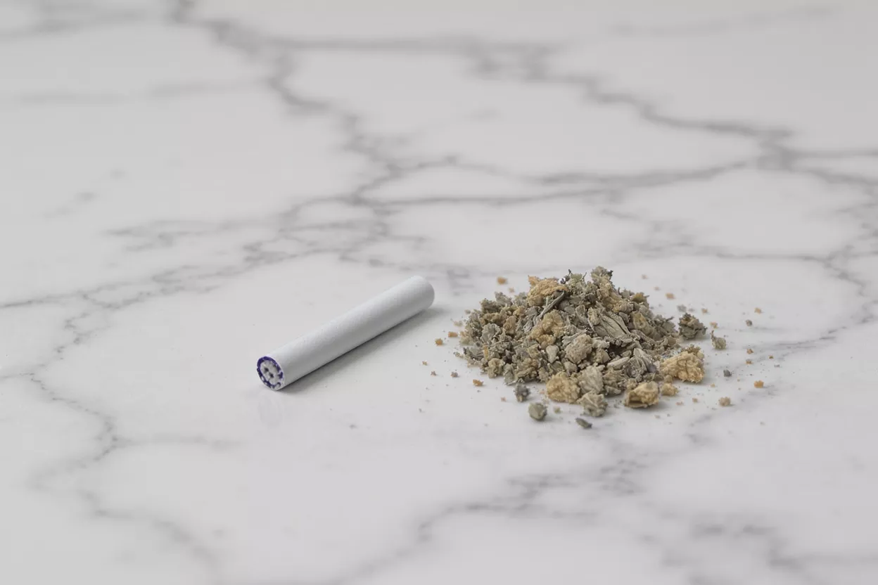 A single extinguished cigarette butt and a pile of ash on a white marble surface.