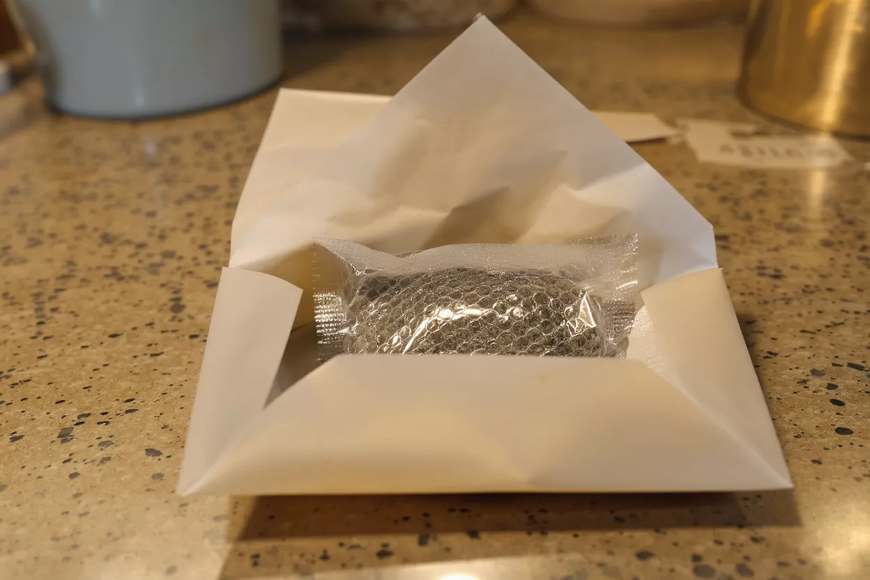 Small item, bubble-wrapped, resting inside a white paper envelope on a speckled counter.