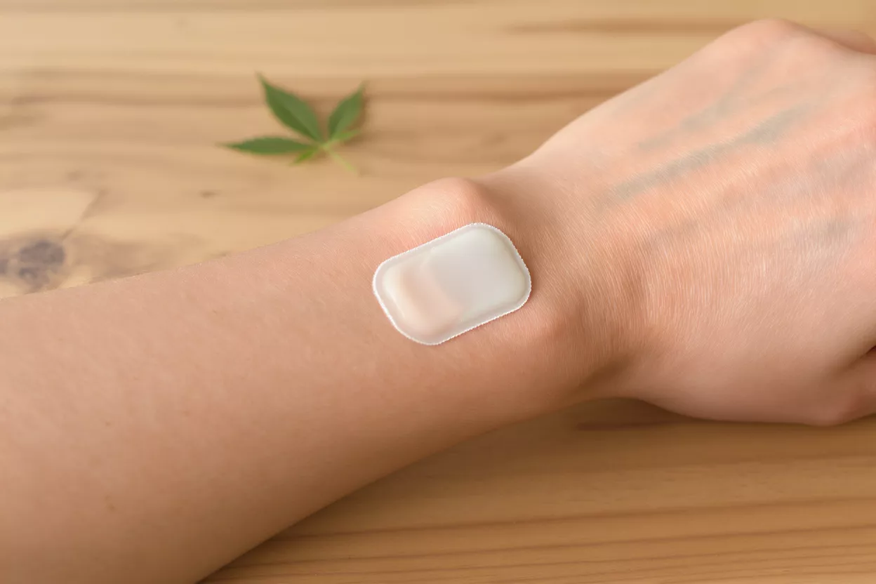 A clear CBD patch applied to a person's wrist, with a cannabis leaf in the background.
