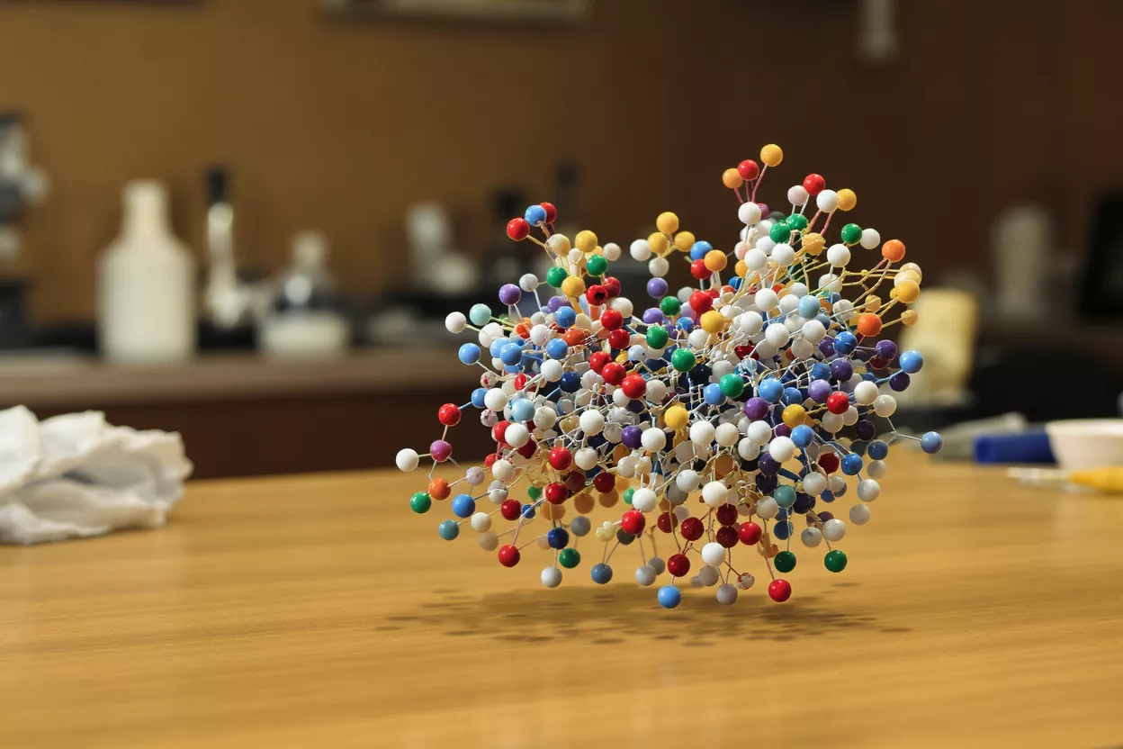 A vibrant, intricate molecular model made of colorful beads on a wooden table.