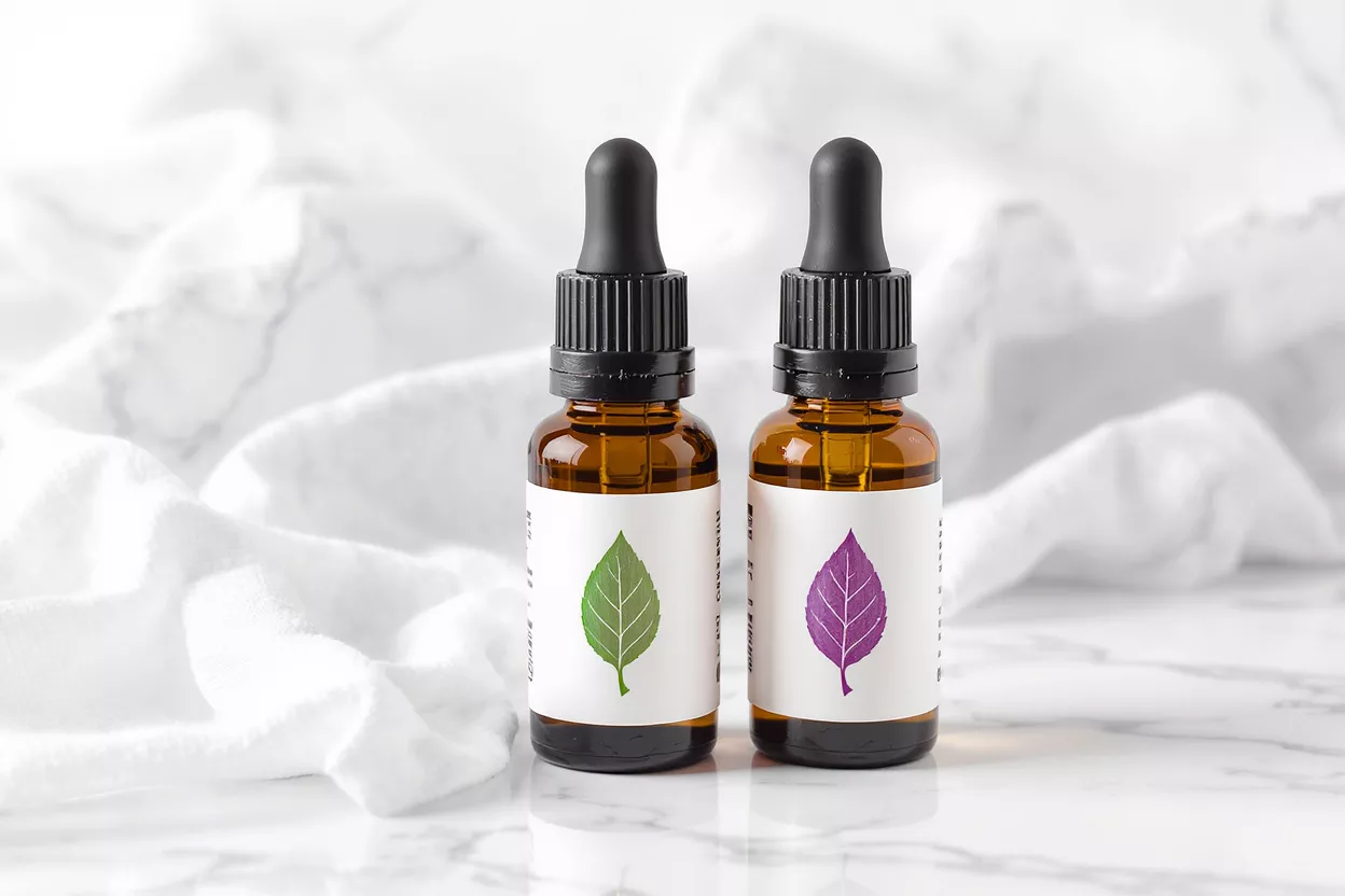 Two amber dropper bottles with leaf labels on marble background with white fabric.