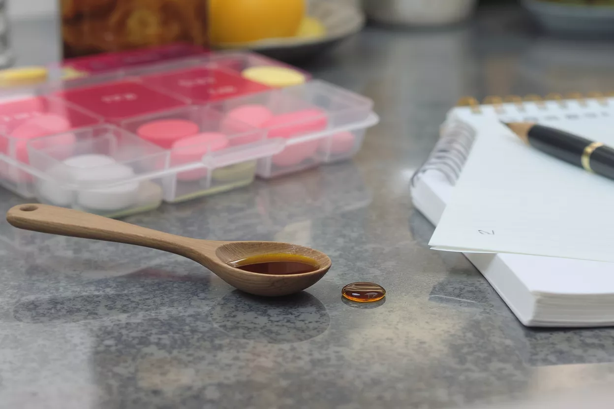 Wooden spoon with liquid medicine, a pillbox, and a notepad with a pen.