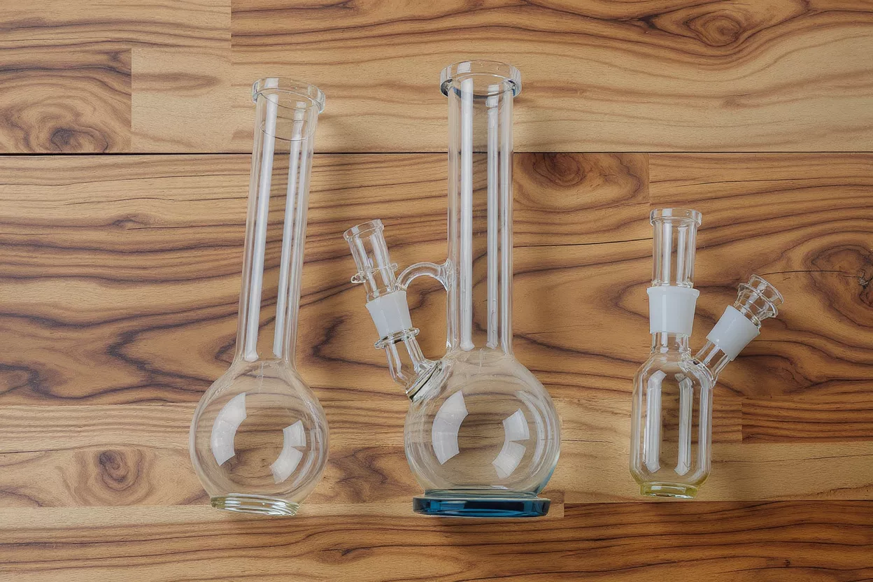 Three clear glass water pipes and bongs on a wooden background.
