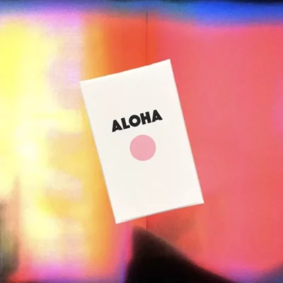 Aloha greeting card with bold text and pink sun on a colorful blurred background.