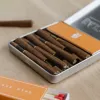 Open tin of pre-rolled cigarillos with matches and orange branding on wooden surface.