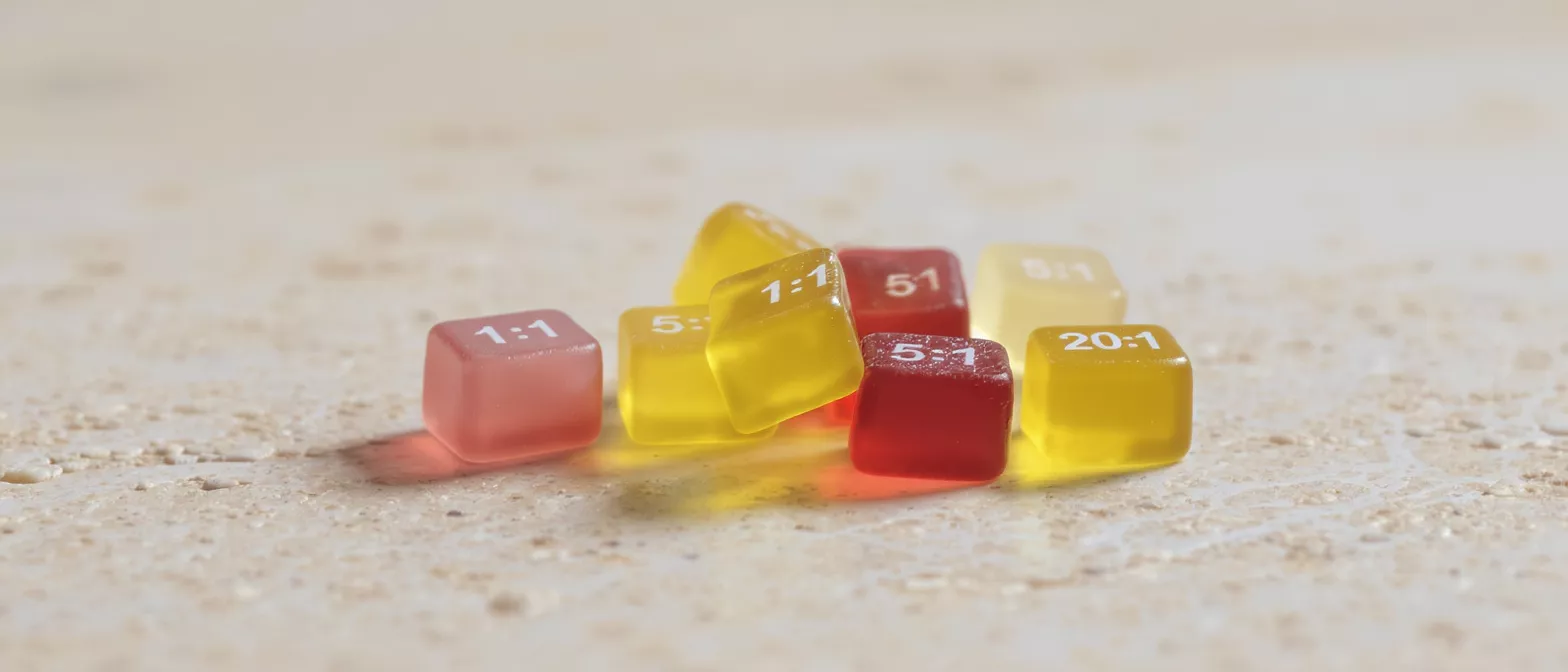 Assorted Ratio Gummies Close-up of red and yellow square gummies with various ratios on a textured surface.