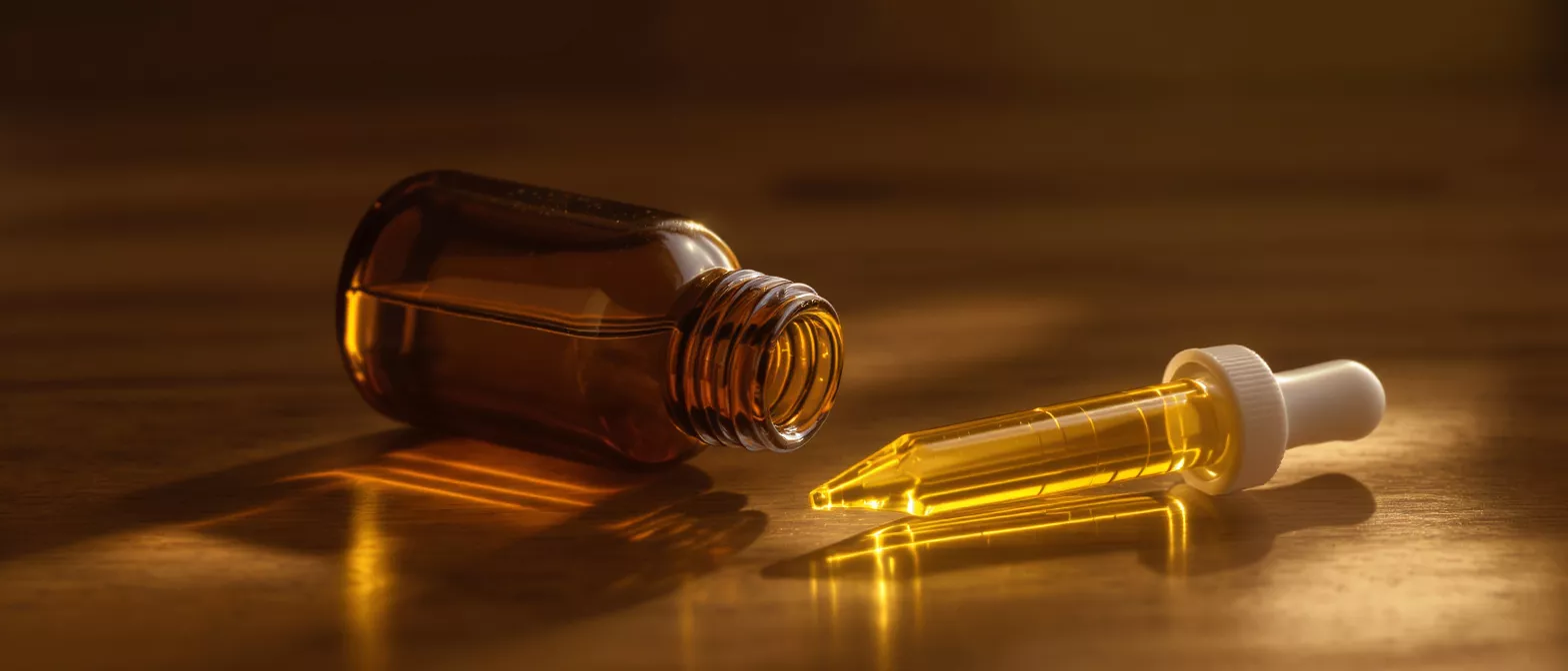 Amber glass bottle and dropper filled with golden liquid on a wooden surface.