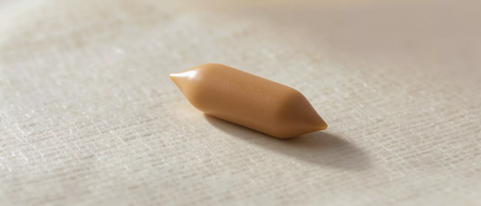 A single, smooth, light brown caramel candy with pointed ends on a textured white surface.