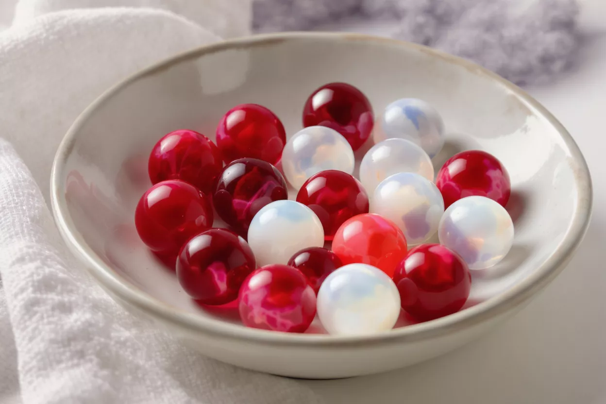 A shallow off-white ceramic bowl filled with glossy red and opalescent white marbles.