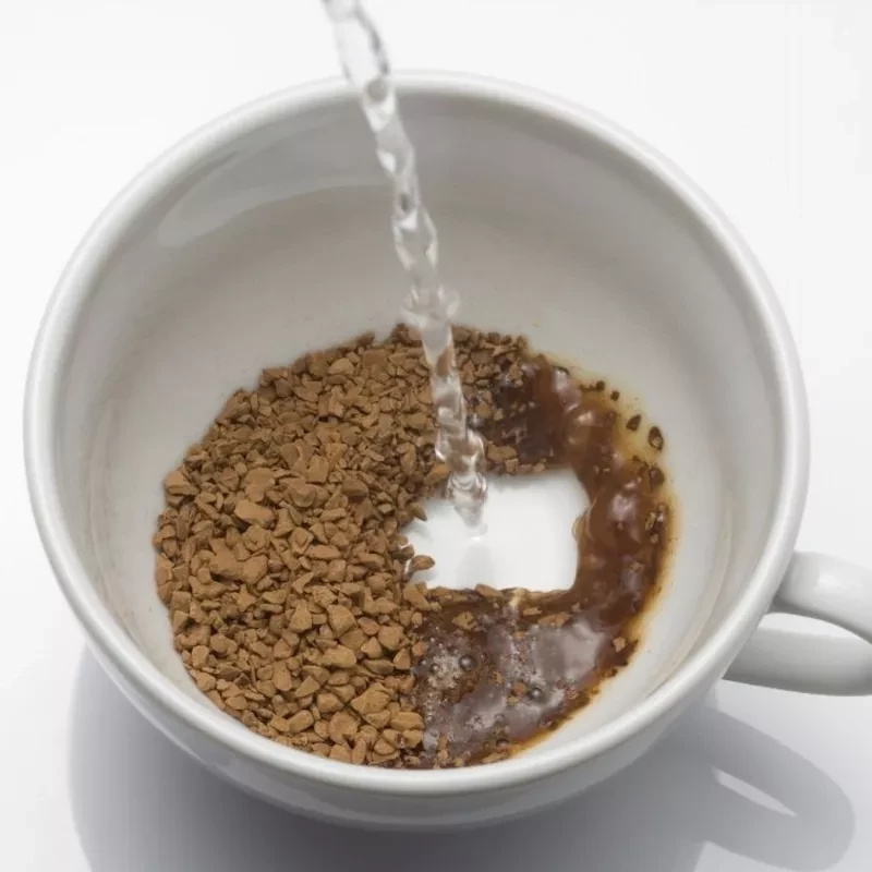 Poring water into mug with instant coffee granules for a quick beverage preparation.