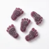 Five purple, foot-shaped gummy candies covered in sugar on a white background.
