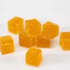 Orange gummy cubes scattered on white surface, sugar-coated, citrus flavor, inviting and vibrant.