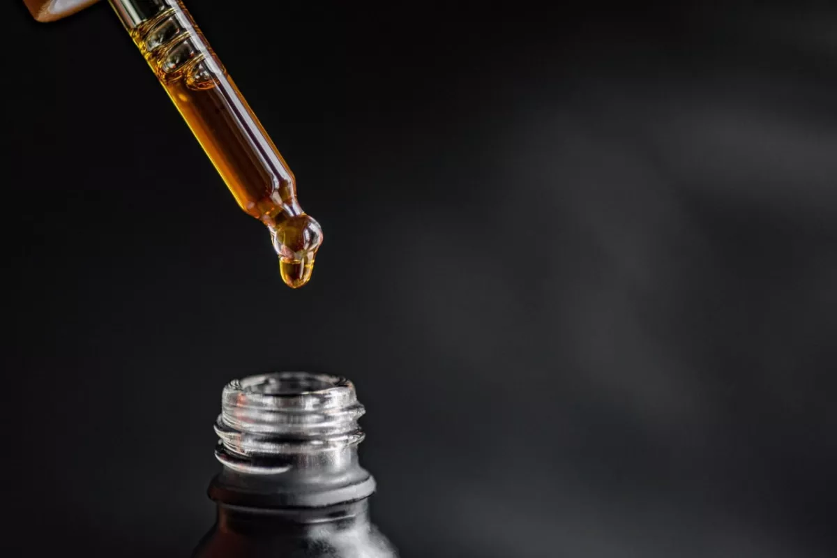 Close-up of golden essential oil being dispensed from dropper into dark bottle.