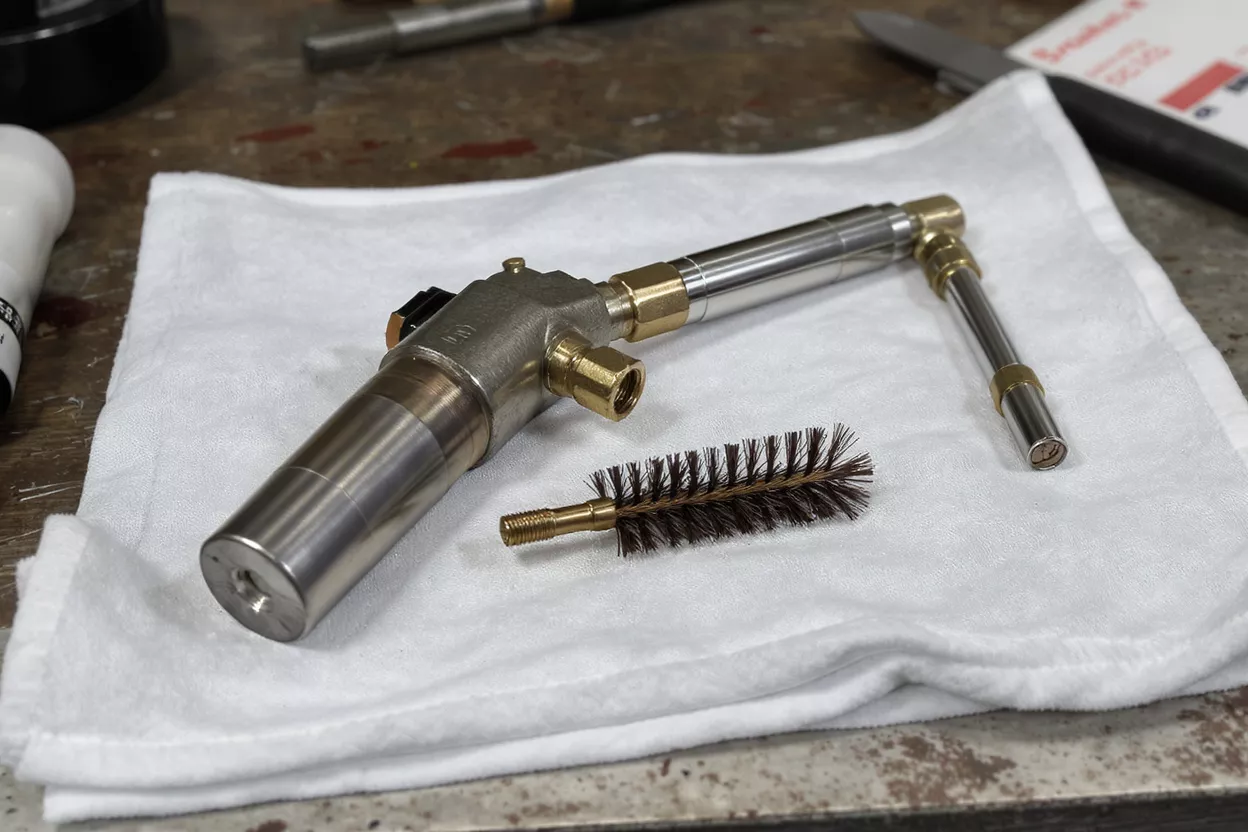 A disassembled metal torch assembly and a wire cleaning brush on a white cloth.