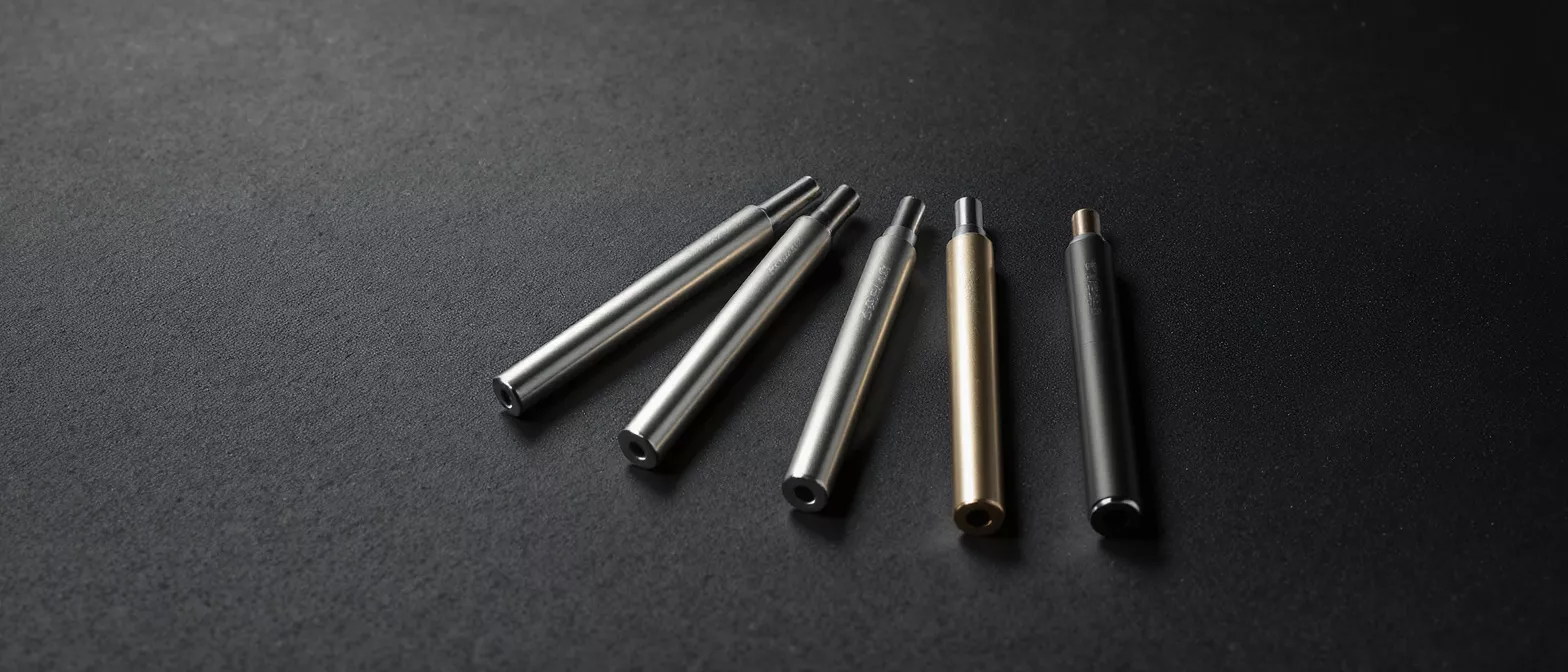 Cinco bolígrafos de metal elegantes en plateado, dorado y negro sobre un fondo oscuro.