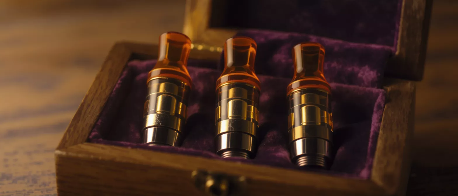 Tres cartuchos de vapeo con puntas ámbar en una caja de madera forrada de terciopelo.