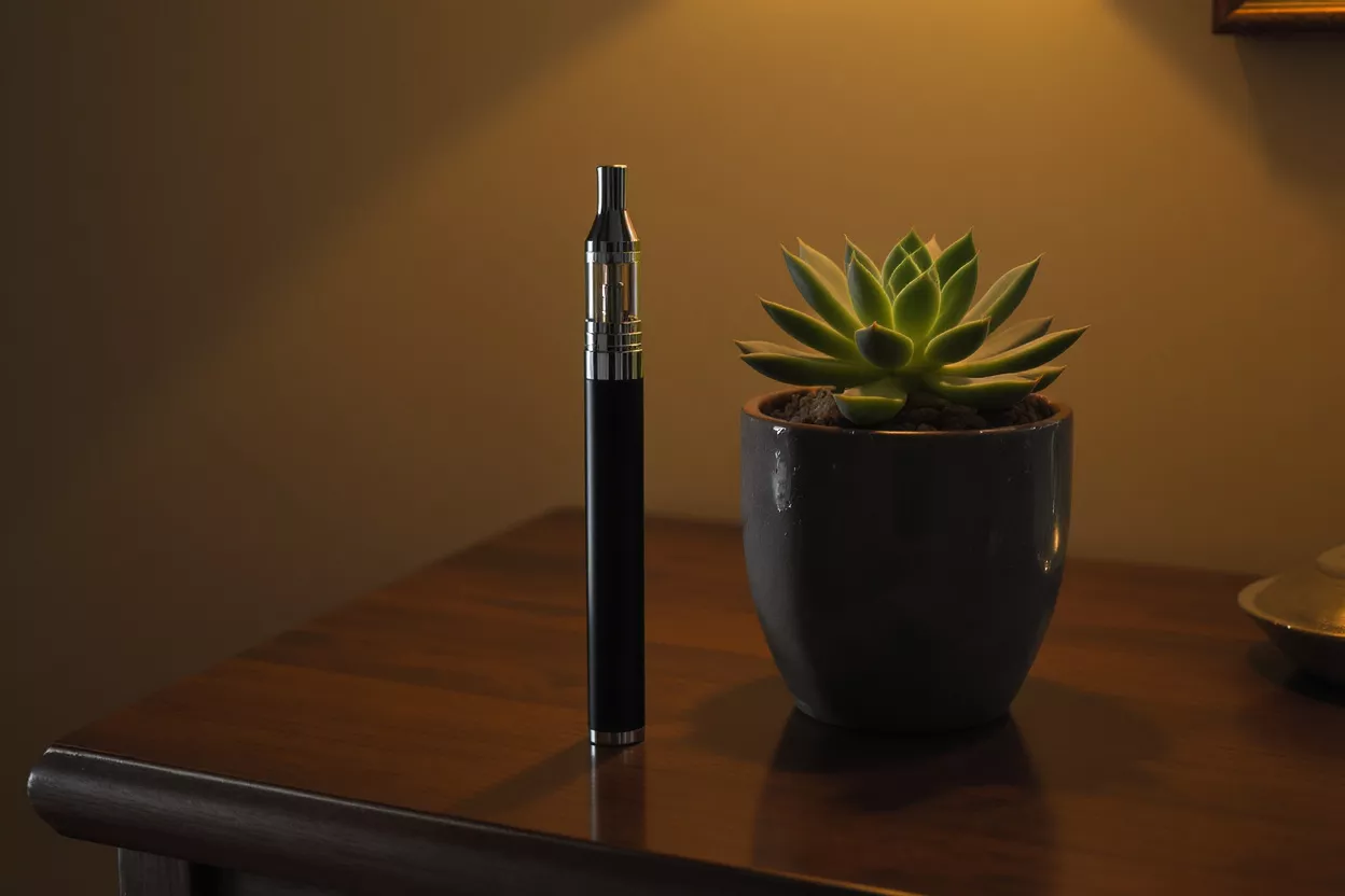 Three vape pens, two silver, one black, on a wooden surface with smoke.
