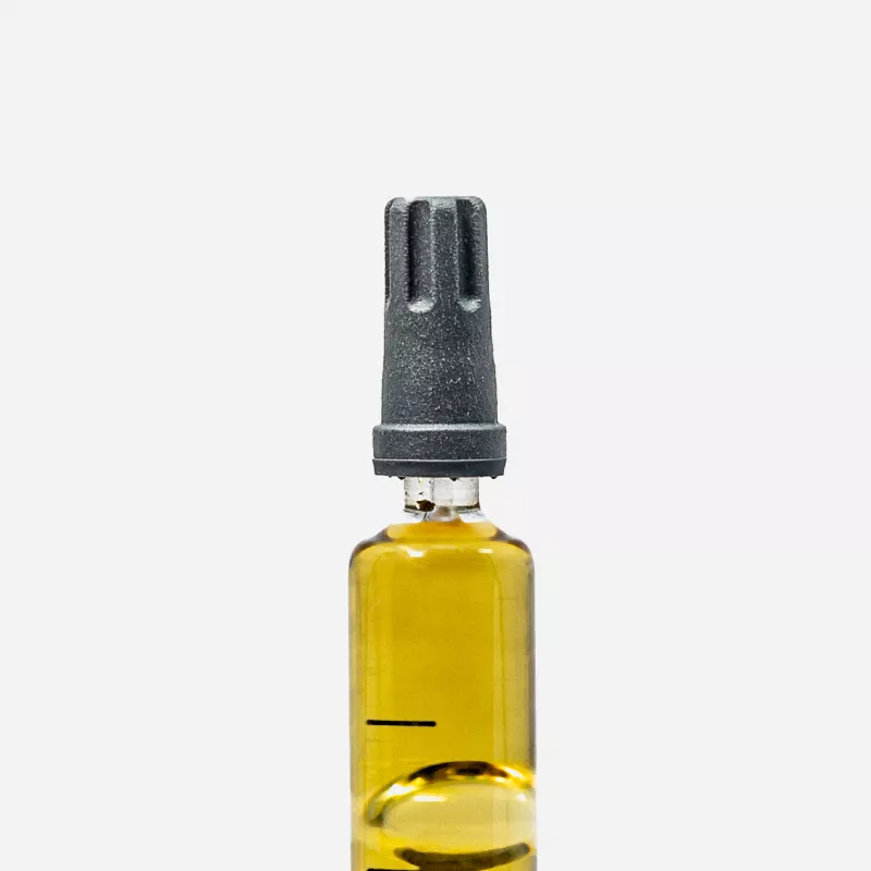 Close-up of medical vial with yellow distillate and needle adapter on white background.