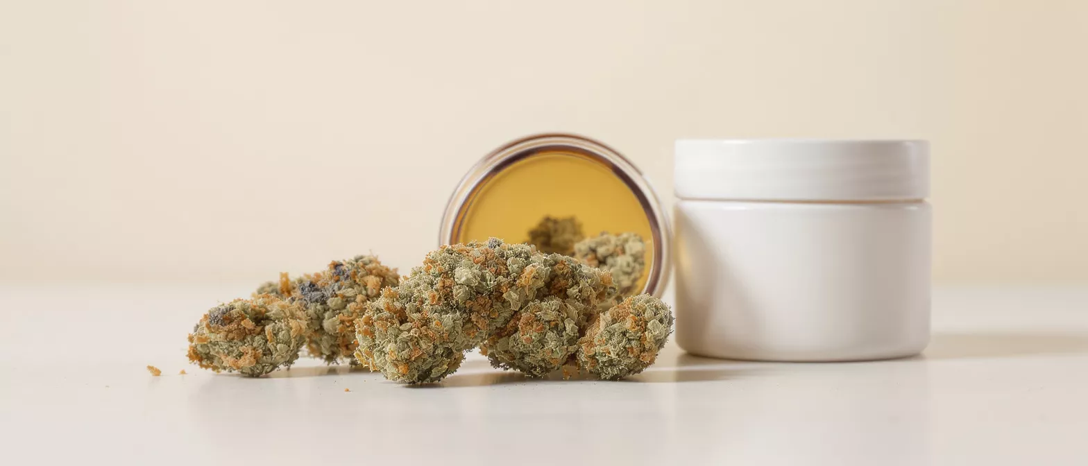 Close-up of cannabis buds spilling from an amber jar next to a white container.
