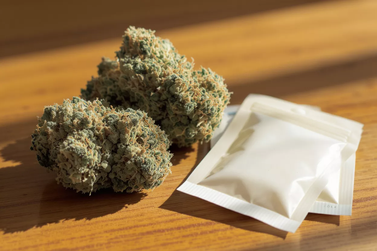 Two cannabis buds and two white humidity control packs on a wooden surface.