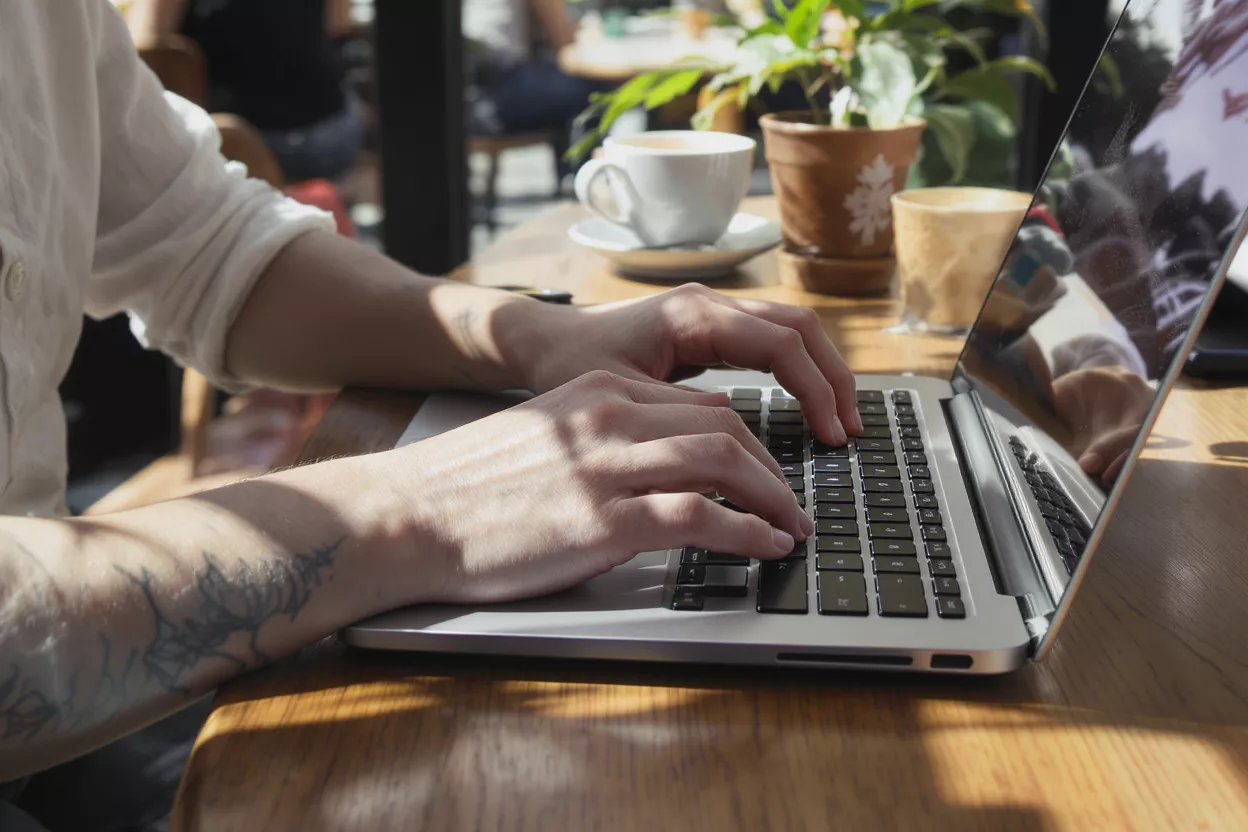 Close-up of hands typing on a laptop keyboard in a cafe setting with coffee.