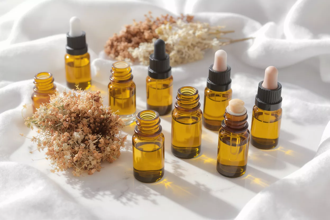 Amber glass bottles with essential oils and droppers, surrounded by dried flowers.