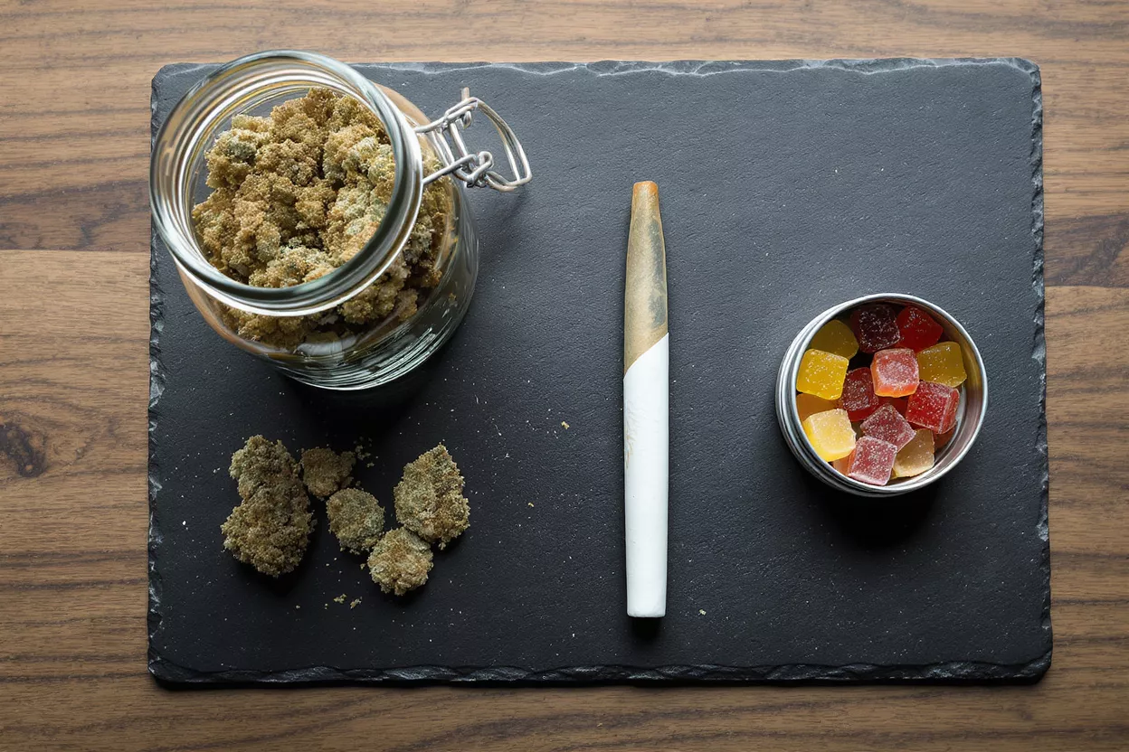 Various cannabis products including flower, pre-roll, and gummies on a dark slate tray.