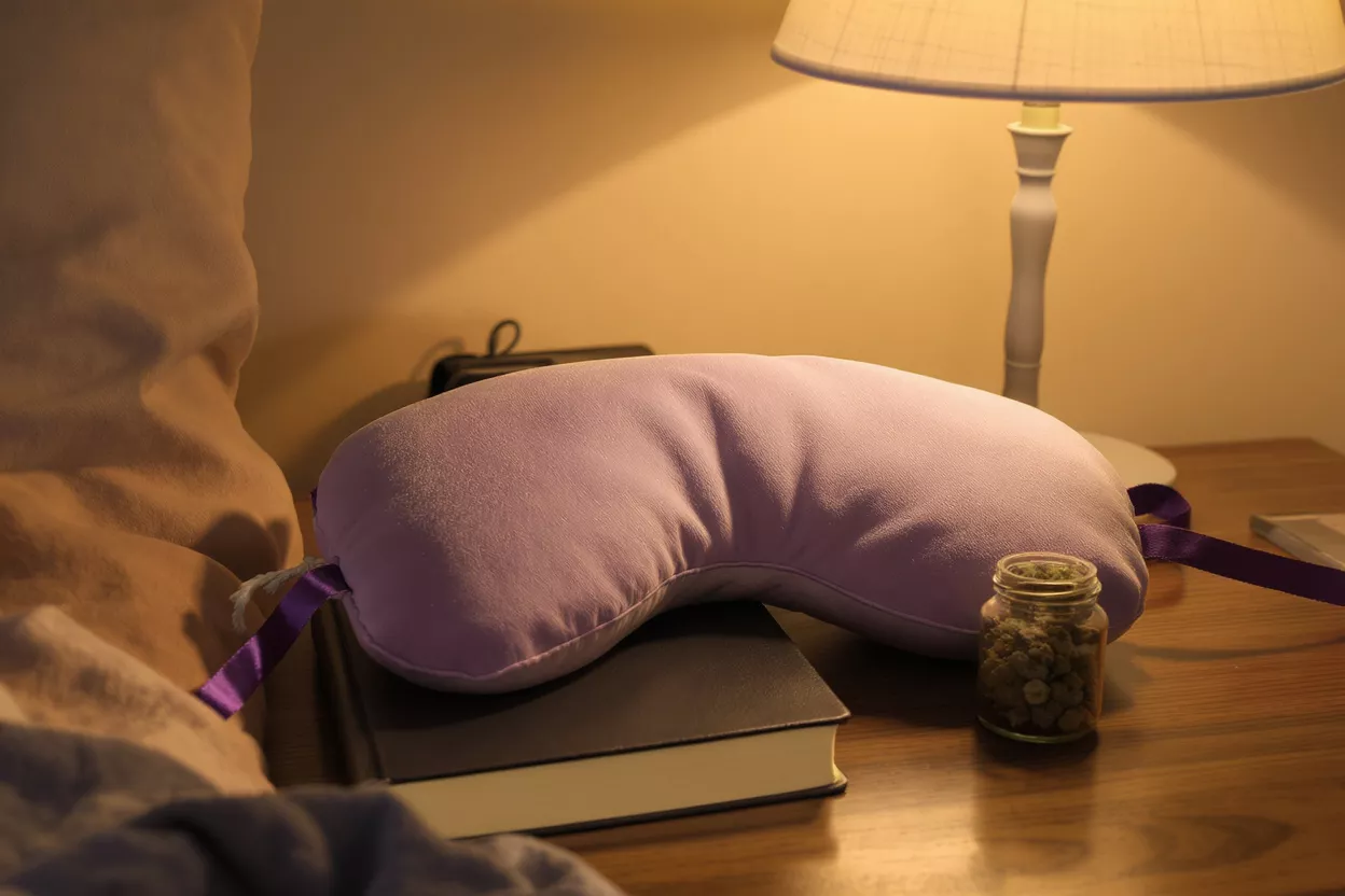 Lavender sleep pillow, book, and jar on a bedside table with a lamp.
