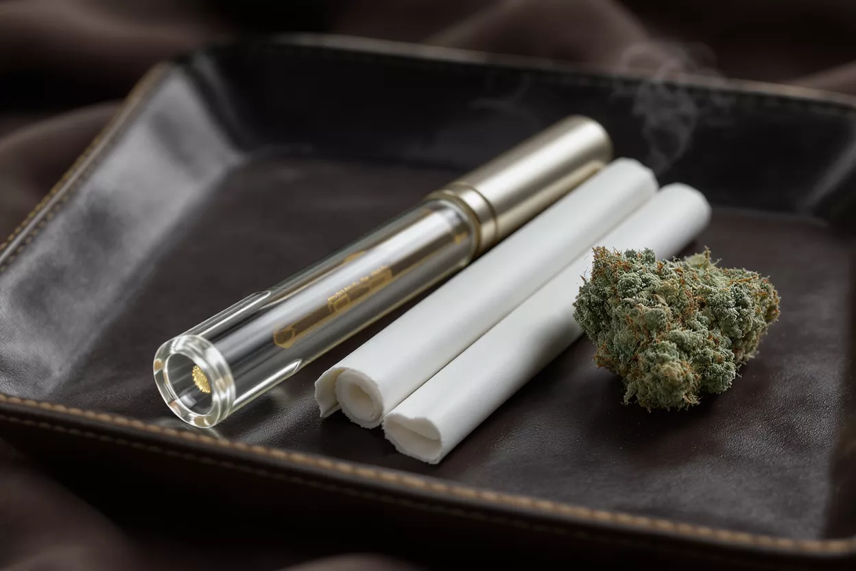 Cannabis bud, glass pipe, and two pre-rolls on a dark brown leather tray.