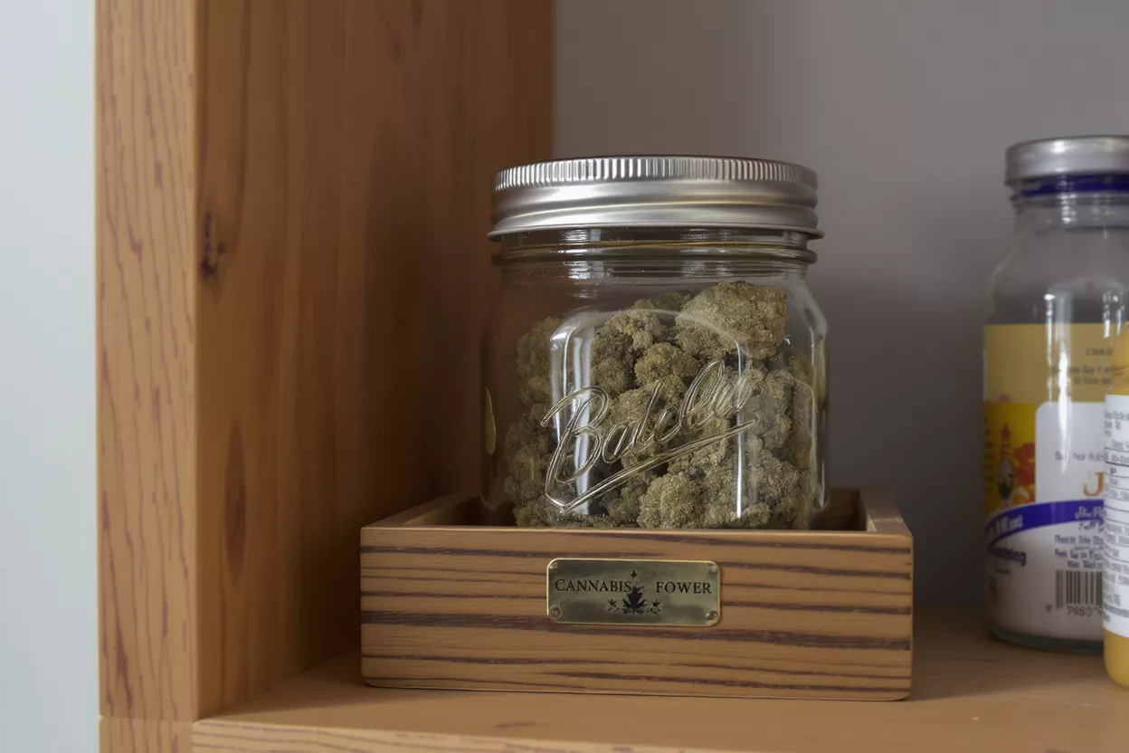 Mason jar filled with cannabis flower on a wooden stand with a 'Cannabis Fower' label.