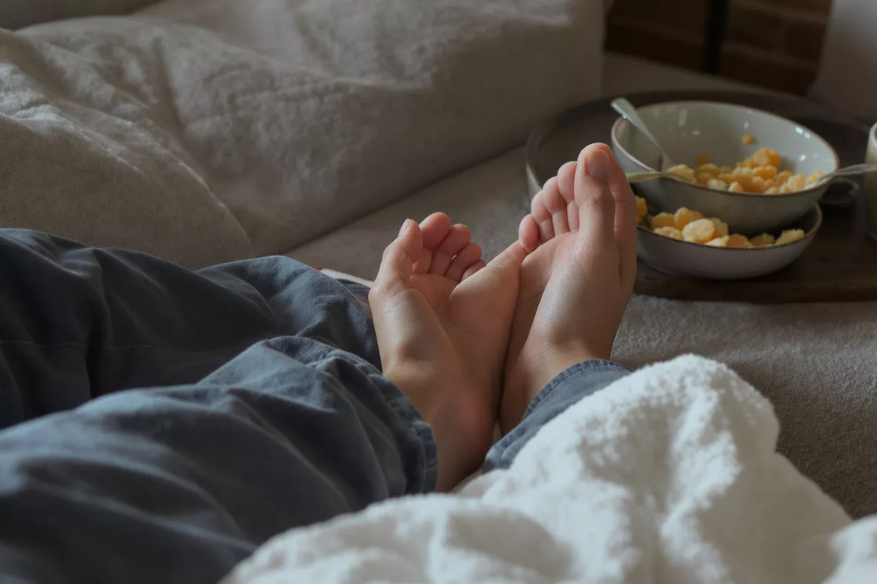 A person's bare feet resting on a bed with a snack bowl nearby.
